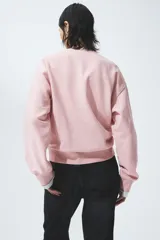 Buzo oversize rosado con interior cepillado suave, cuello redondo, hombros caídos y estampa frontal con la inscripción 'New York Pilates Club'. Cuenta con ribetes acanalados en el cuello, los puños y el bajo.