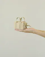 Charm o llavero en forma de mini bolso, color beige, con doble asa superior y cierre de cremallera con mosquetón metálico dorado.
