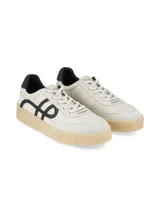 Championes de estilo urbano en color crema con detalles en negro. Presentan un diseño con logo lateral curvo, puntera de gamuza y suela de goma texturizada en tono natural.