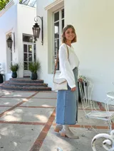 Cartera tipo sobre color crudo, confeccionada en cuero, con correa larga de cuero marrón y costuras decorativas en contraste.