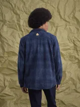 Sobrecamisa de tejido polar con estampado abstracto en tonos rojizos y azul marino. Presenta cuello clásico, cierre frontal con botones a presión, dos bolsillos frontales con solapa en el pecho y un parche decorativo.