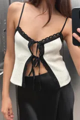 Top corto de tejido acanalado color blanco, con escote pico, tirantes finos negros y ribetes de encaje negro en el escote y el ruedo. Presenta un cierre frontal con lazada ajustable.