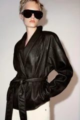 Chaqueta ZARA Woman Collection efecto piel en color marrón oscuro, de manga larga y cuello smoking. Cuenta con cinturón ajustable del mismo material para atar en la cintura y forro interior.