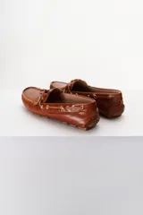 Mocasines plateados de cuero con cordones decorativos y suela de goma marrón.