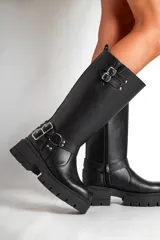 Borcegos negros de ecocuero con caña alta y base con plataforma. Presentan correas con hebillas plateadas en la parte superior y alrededor del tobillo.