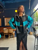 Campera corta de cuerina negra con mangas turquesas metalizadas y detalles plateados en cuello y puños.