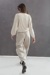 Buzo de lanilla color arena con cuello alto, mangas abullonadas y puños elásticos. Presenta un detalle de cinta tejida trenzada aplicada alrededor de la sisa.