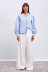 Blusa celeste con rayas verticales, cuello en V, mangas largas abullonadas con puños blancos y volantes verticales en el frente.