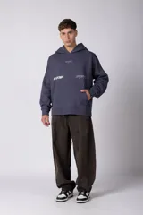 Buzo canguro negro con capucha, confeccionado en algodón frizado de alto gramaje. Presenta estampado gráfico en el pecho con tipografía cursiva y texto, además de un logo circular en la manga. Cuenta con bolsillo frontal tipo canguro, puños y ruedo acanalados.