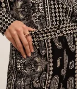 Pantalón largo de corte ancho con estampado paisley en tonos blanco y negro. Presenta cintura alta con trabillas, cierre frontal tradicional y confección en tejido viscolino, una mezcla de lino y viscosa.