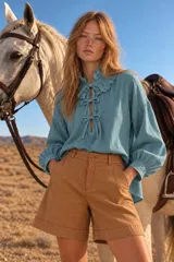 Blusa blanca de manga larga con cuello alto y volados, cierre frontal con lazos y diseño holgado.