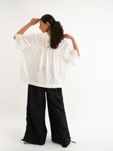 Pantalón negro de lino con cintura elástica fruncida y pernera ancha, con detalles de cordones ajustables a los lados.
