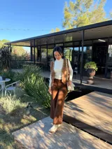 Cartera tipo bandolera de cuero color crudo, con diseño rectangular, solapa frontal con detalle de costura decorativa en el borde y correa ajustable.