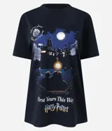 Remera negra de algodón con cuello redondo, mangas cortas y estampa frontal de la saga Harry Potter con ilustración nocturna del castillo de Hogwarts y el texto First Years This Way.