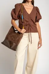 Blusa marrón de algodón con bordados sutiles, escote en V, mangas cortas abullonadas y detalle de fruncido con cordón ajustable en el centro del frente.