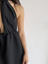 Vestido corto negro con escote halter y espalda descubierta. Presenta un corte a la cintura con falda acampanada.