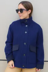 Campera de paño azul con cuello alto, cierre frontal de botones y bolsillos laterales con solapa en tono más oscuro. Presenta puños en contraste y un diseño estructurado.
