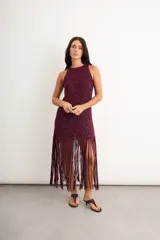 Vestido midi de crochet bordó con destellos de lurex, de cuello redondo y sin mangas, con falda terminada en largos flecos trenzados a mano.
