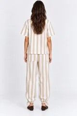 Pantalón a rayas beige y blancas con cintura elástica, bolsillos laterales y traseros, corte holgado con piernas globo y cordón de ajuste en los tobillos.