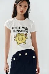 Camiseta de algodón flamé color blanco, de corte regular con cuello redondo y manga corta. Presenta un estampado frontal con texto y gráfico del personaje Little Miss Sunshine.