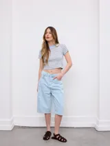 Bermuda de jean de tiro alto, color celeste claro, con diseño amplio y largo por debajo de las rodillas. Cuenta con bolsillos clásicos y costuras pespunteadas en contraste.