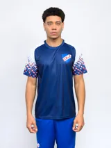 Remera deportiva de entrenamiento para hombre, color azul marino, con cuello redondo. Las mangas y los hombros son blancos, con un patrón de mosaico en tonos rojo, blanco y azul que se desvanece hacia el centro. Lleva el escudo del Club Nacional de Football en el pecho.