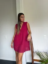 Vestido corto color fucsia, con escote en V profundo y mangas cortas tipo volado. Presenta un diseño con textura de bordado inglés o perforado y un corte imperio con frunce que da volumen a la falda.