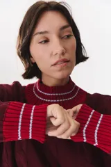 Buzo de tejido de punto con diseño de trenzas, color crema con detalles en marrón en cuello, puños y ruedo. Presenta líneas finas en contraste y pequeñas costuras decorativas en forma de cruz.