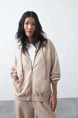 Campera con capucha y cierre frontal, de silueta relajada, hombros caídos y bolsillos laterales. Presenta terminaciones elastizadas en puños y ruedo, con líneas de recorte frontales y cierre metálico con tirador circular.