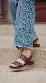 Sandalias planas de cuero color marrón chocolate, con dos tiras anchas en el empeine decoradas con costuras artesanales y tira ajustable con hebilla en el talón.
