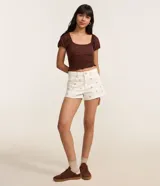 Short slim de talle medio confeccionado en sarga de algodón color marfil, con trabillas en la cintura, cierre tradicional con botón y cremallera, bolsillos, dobladillo deshilachado y delicados bordados florales repartidos por toda la prenda.