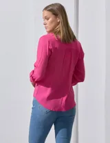 Blusa blanca de gasa marca Zac & Rachel, con cuello a la base, escote en V, abertura central con botones, bolsillo aplicado en el pecho y mangas largas regulables con presilla y botón. Tiene terminación opcional de nudo en el ruedo.