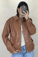 Chaqueta de ecocuero color marrón, de corte oversize, con cuello clásico, cierre frontal metálico, bolsillos laterales con solapa y puños con broches a presión.