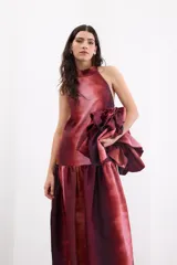 Vestido largo de corte holgado con estampado degradé en tonos rojizos y bordó. Presenta escote halter con cuello alto, espalda descubierta con cierre de botones y un maxi volado en la cadera que aporta volumen a la falda.