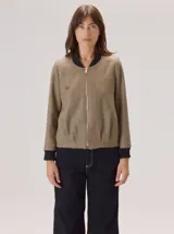 Chaqueta tipo bomber de lana con estampado de espiga en tonos grises. Presenta cuello, puños y ruedo en tejido elástico negro, cierre frontal dorado y bordado sutil en el pecho.