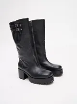 Bota bucanera de cuero vacuno wax color negro, con punta cuadrada, suela de goma con plataforma dentada y taco de madera. Presenta detalle de doble hebilla metálica en la parte superior de la caña.