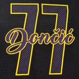 Remera deportiva negra con cuello en V y mangas cortas, confeccionada en tejido tipo malla transpirable. Presenta el nombre "Lakers" bordado en el pecho con letras amarillas y bordes morados y blancos. En la parte inferior cuenta con un gráfico impreso que simula el horizonte de una ciudad en tonos grises y morados, y detalles de líneas amarillas y moradas en el cuello y los puños.