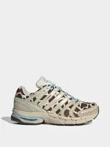 Championes Adidas Adistar Control 5 con diseño de estampado animal print tipo vaca en tonos marrón y blanco. Presenta detalles en color beige, acentos en celeste en los cordones y la entresuela, y estructura reforzada con paneles laterales.
