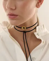 Choker de estilo bolo tie compuesto por un cordón negro largo y un dije central ovalado con diseño de estrella calada en acabado dorado espejado.