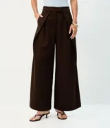 Pantalón de sastrería en crepé color marrón, de modelaje barrel y tiro alto con cintura estructurada. Presenta pinzas frontales profundas, bolsillos embutidos y caída amplia de corte recto.