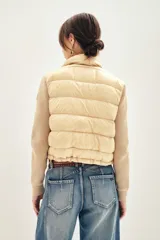 Campera puffer color beige con cuerpo acolchado y mangas tejidas de punto. Presenta cuello alto, cierre frontal y bolsillos laterales.
