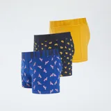 Pack de tres boxers para hombre. Incluye un boxer amarillo liso, un boxer azul marino con estampado de patos amarillos y un boxer azul con estampado de flamencos rosados. Todos tienen cintura elástica con la palabra "ULTIMATE" grabada.