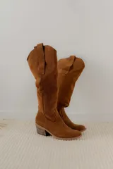 Bota estilo tejana de caña alta, confeccionada en gamuza, con taco cuadrado y diseño de costuras decorativas.