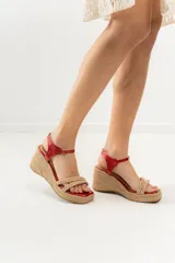Sandalias de taco chino con plataforma revestida en yute natural. Posee capellada de tiras cruzadas de yute en la parte delantera, puntera cuadrada y tira ajustable de cuero rojo metalizado en el talón.