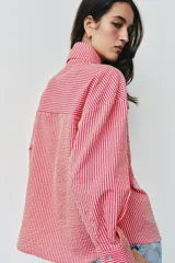 Camisa de rayas rosadas y blancas, con cuello subido decorado con un lazo integrado, manga larga con puños abotonados y cierre frontal oculto.