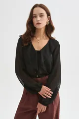 Blusa blanca de poliéster con cuello en V, volados frontales y mangas largas con elástico en los puños.