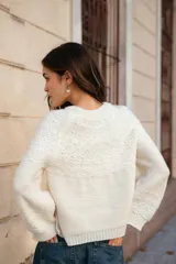 Buzo tejido de punto con cuello redondo, manga larga y diseño holgado. Presenta tajos laterales y un corte asimétrico, siendo ligeramente más largo en la parte posterior.