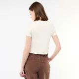 Camiseta corta de canalé en color blanco, de manga corta y cuello redondo, con detalles de pequeños nudos decorativos en el lateral.