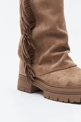 Bota de caña media con flecos laterales, confeccionada en material con textura tipo gamuza. Presenta una silueta relajada y suela robusta con base dentada.