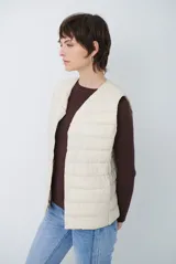 Chaleco acolchado tipo puffer, color beige, sin mangas, con cuello redondo y cierre frontal con botones a presión.